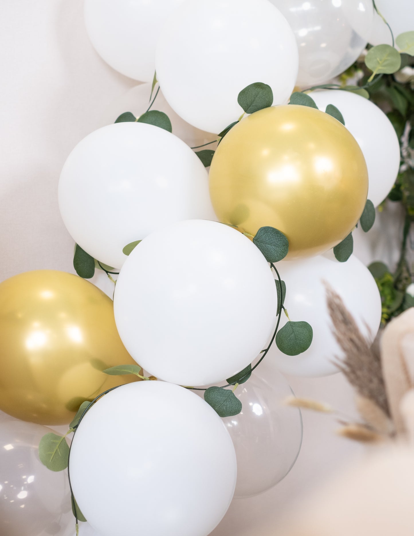 Gros plan sur les ballons et le feuillage du kit arche de 60 ballons blanche et or avec eucalyptus végétale
