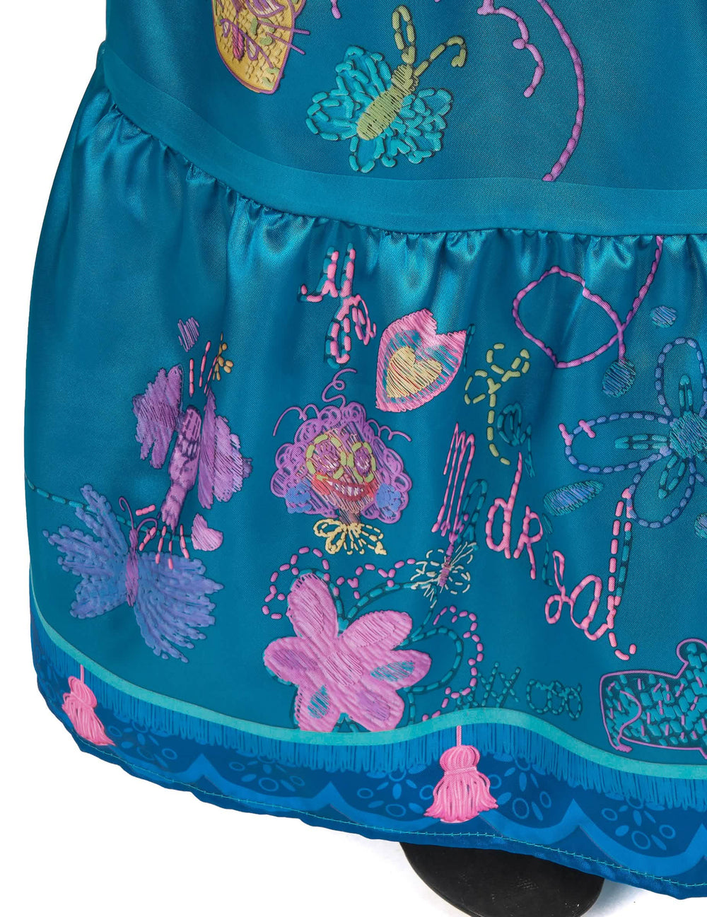 Gros plan sur les pompons et broderies du bas de la jupe du déguisement Mirabel deluxe Encanto™